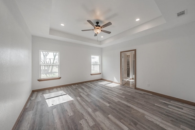 unfurnished room with wood finished floors, a raised ceiling, visible vents, and baseboards