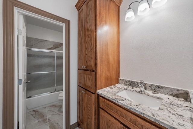 full bath featuring marble finish floor, shower / bath combination with glass door, vanity, and toilet