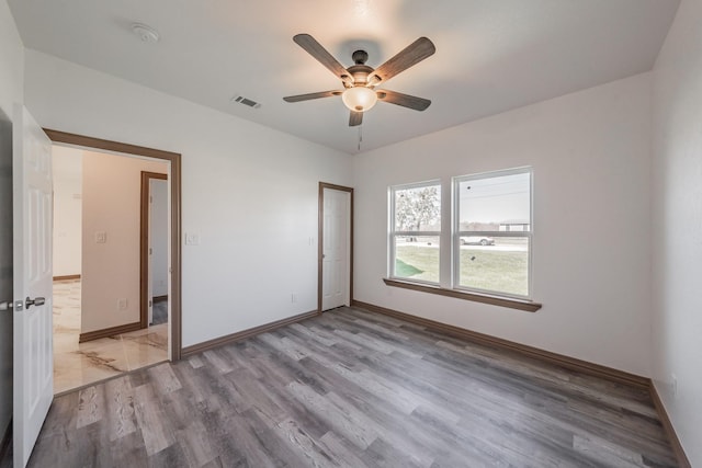 empty room with light wood-type flooring, visible vents, ceiling fan, and baseboards