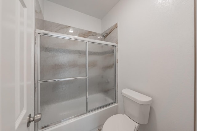 bathroom featuring toilet and shower / bath combination with glass door