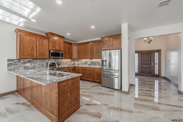 kitchen featuring marble finish floor, brown cabinets, stainless steel appliances, a sink, and a peninsula