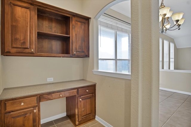 unfurnished office with arched walkways, built in study area, baseboards, and light tile patterned floors