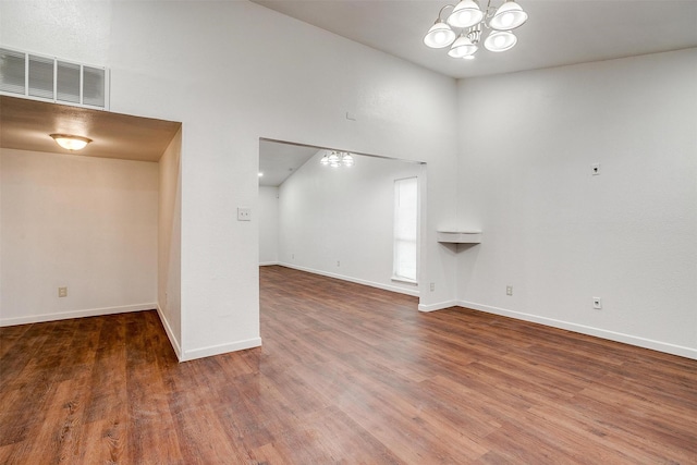 unfurnished living room featuring a chandelier, visible vents, baseboards, and wood finished floors