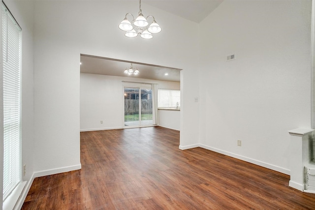 unfurnished living room with baseboards, visible vents, a towering ceiling, wood finished floors, and a chandelier