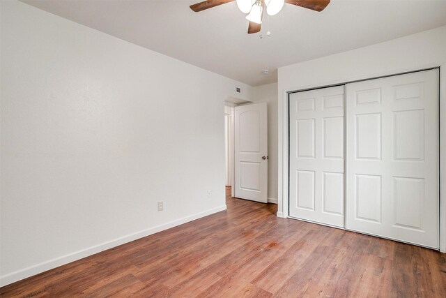 unfurnished bedroom featuring ceiling fan, a closet, baseboards, and wood finished floors