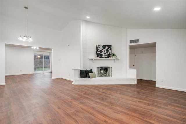 unfurnished living room featuring a fireplace, a notable chandelier, visible vents, wood finished floors, and baseboards