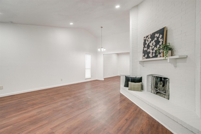 living area with wood finished floors, baseboards, vaulted ceiling, a brick fireplace, and an inviting chandelier