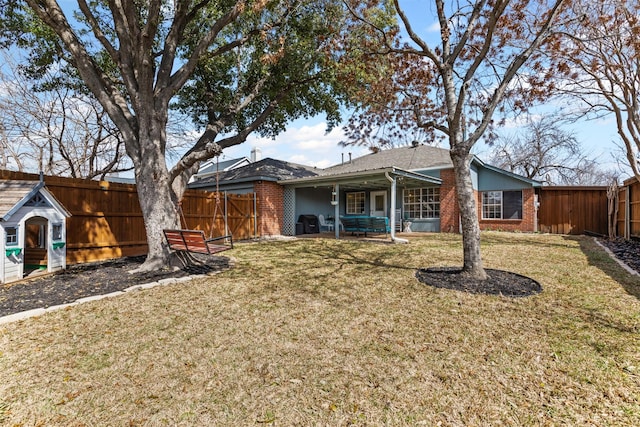 back of house featuring a yard, brick siding, and a fenced backyard