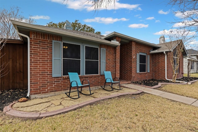 rear view of property with a yard, a chimney, fence, and brick siding