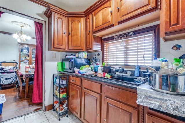 kitchen featuring black microwave, decorative backsplash, brown cabinets, an inviting chandelier, and a sink