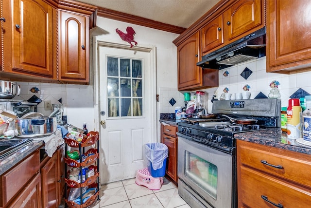 kitchen featuring under cabinet range hood, brown cabinets, dark stone counters, and stainless steel range with gas cooktop