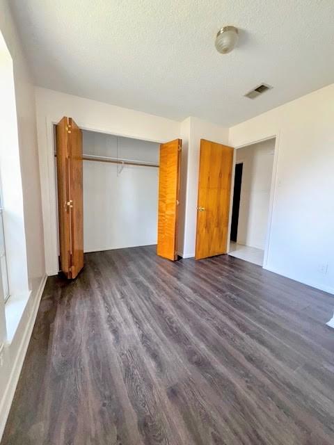 unfurnished bedroom with dark wood-style floors, a closet, visible vents, and a textured ceiling