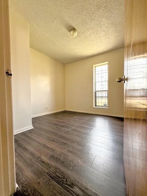 spare room with a textured ceiling, baseboards, and dark wood-style flooring