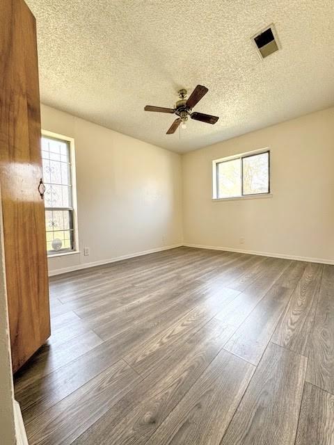 unfurnished room with ceiling fan, plenty of natural light, wood finished floors, and visible vents