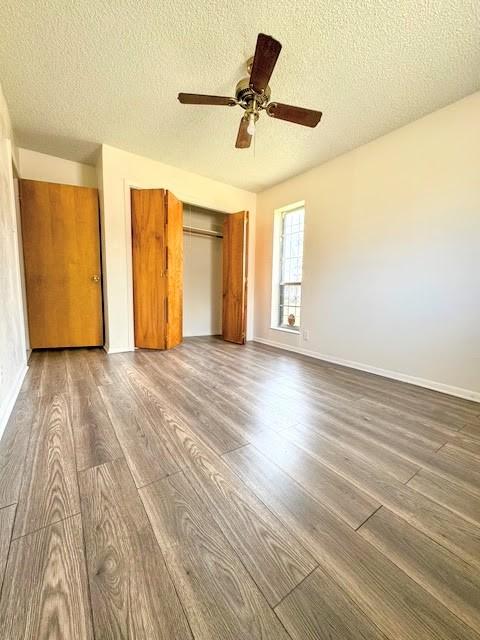 unfurnished bedroom featuring baseboards, ceiling fan, dark wood-type flooring, a textured ceiling, and a closet