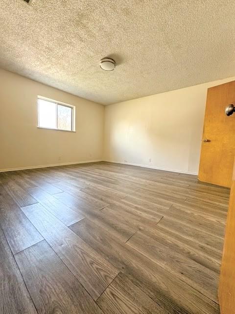 spare room featuring a textured ceiling, baseboards, and wood finished floors