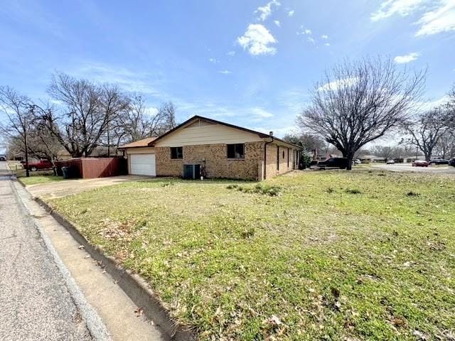 view of side of property featuring a garage, concrete driveway, a yard, central AC, and brick siding