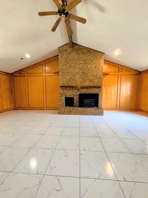 unfurnished living room with lofted ceiling with beams, wooden walls, a ceiling fan, marble finish floor, and a brick fireplace