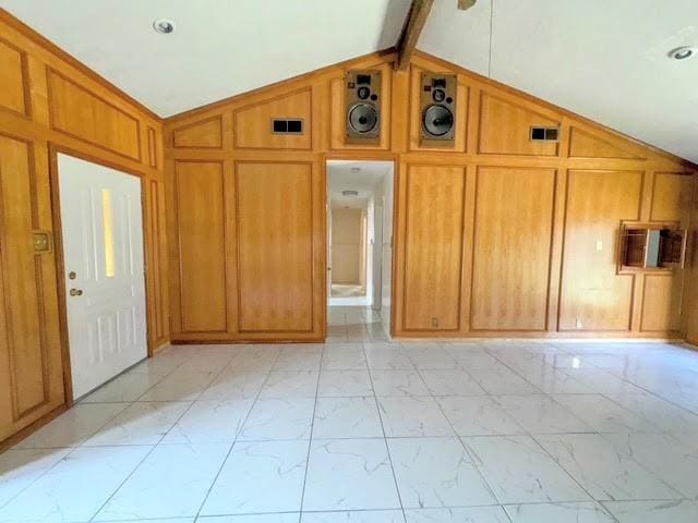 interior space featuring vaulted ceiling with beams, marble finish floor, and wood walls