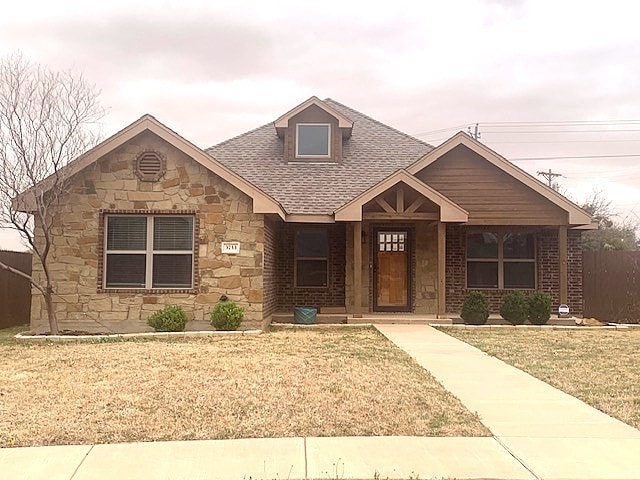 view of front facade with stone siding, roof with shingles, and a front yard