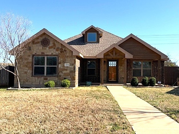 view of front of house with stone siding, fence, and a front yard