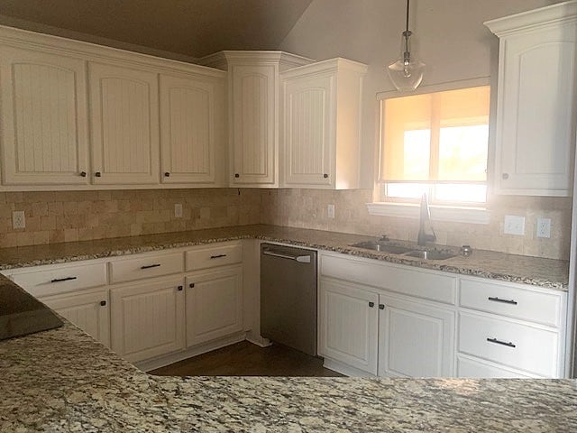 kitchen with a sink, white cabinets, stainless steel dishwasher, backsplash, and light stone countertops