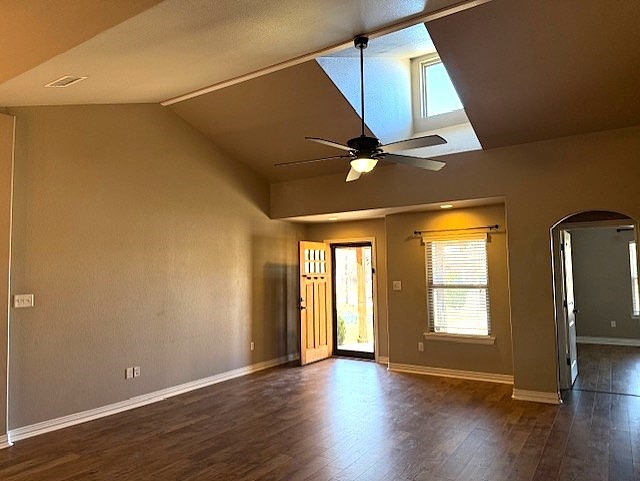 unfurnished room with arched walkways, lofted ceiling, dark wood-style flooring, a ceiling fan, and baseboards