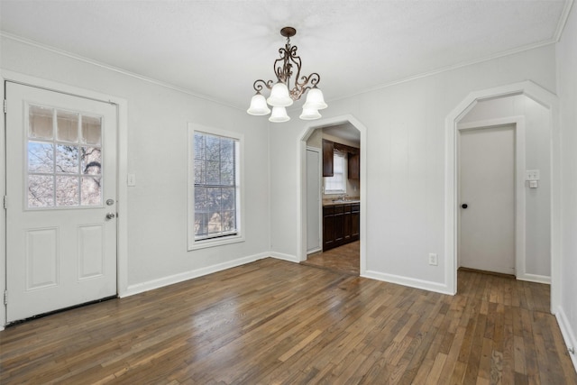 unfurnished dining area featuring a chandelier, arched walkways, dark wood-type flooring, and crown molding