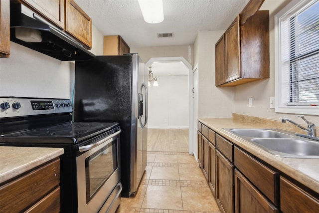 kitchen featuring arched walkways, under cabinet range hood, a sink, visible vents, and stainless steel range with electric stovetop