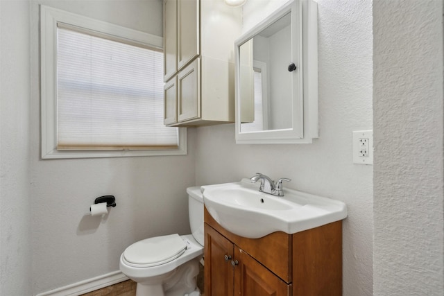 bathroom with a textured wall, vanity, and toilet