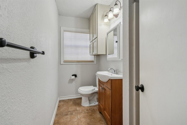 half bathroom featuring toilet, a textured wall, baseboards, and vanity