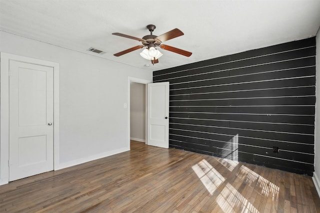 empty room featuring a ceiling fan, wood finished floors, visible vents, and baseboards