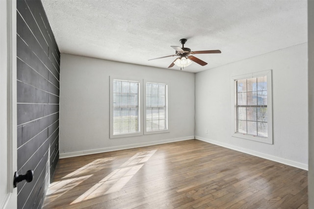 unfurnished room with a textured ceiling, wood finished floors, a ceiling fan, and baseboards