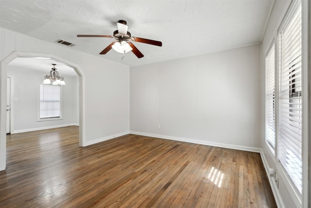 unfurnished room featuring arched walkways, visible vents, plenty of natural light, and hardwood / wood-style flooring