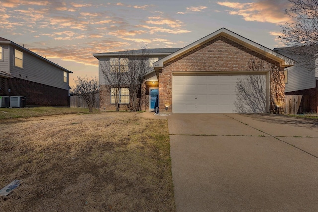 view of front of property featuring brick siding, a lawn, a garage, cooling unit, and driveway