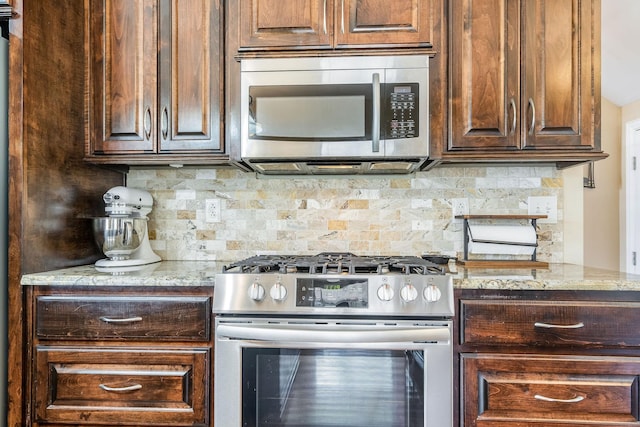 kitchen with light stone countertops, dark brown cabinets, stainless steel appliances, and decorative backsplash