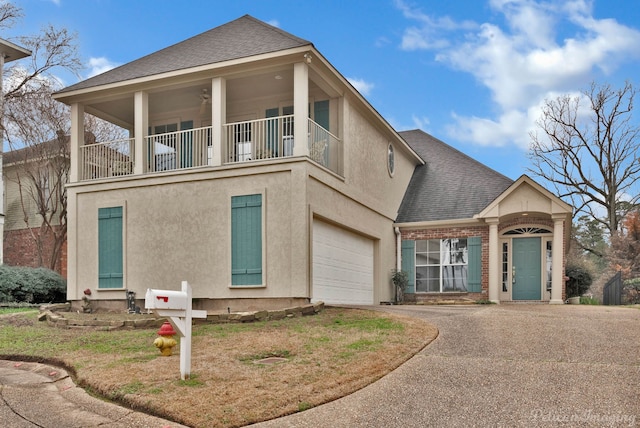 view of front of house with driveway, brick siding, a shingled roof, a balcony, and stucco siding