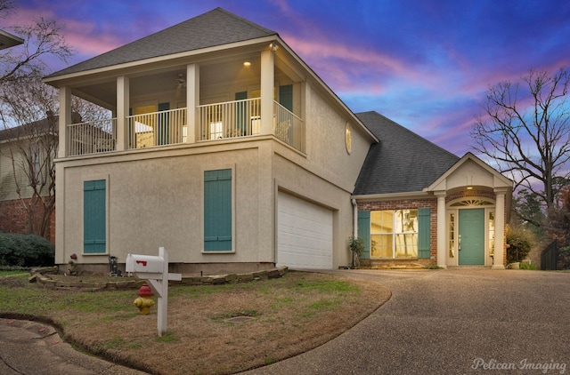 traditional-style home featuring a shingled roof, an attached garage, driveway, and a balcony