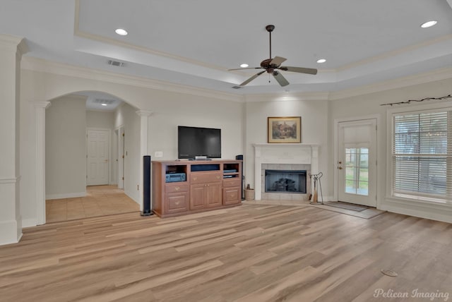 unfurnished living room featuring arched walkways, decorative columns, a raised ceiling, light wood-style floors, and a tile fireplace