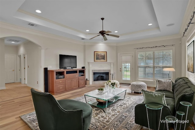 living room featuring visible vents, a raised ceiling, arched walkways, a ceiling fan, and light wood finished floors