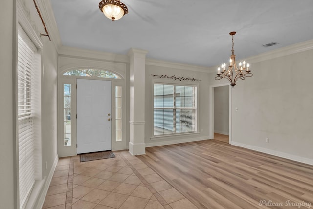 foyer entrance with visible vents, baseboards, crown molding, and a notable chandelier
