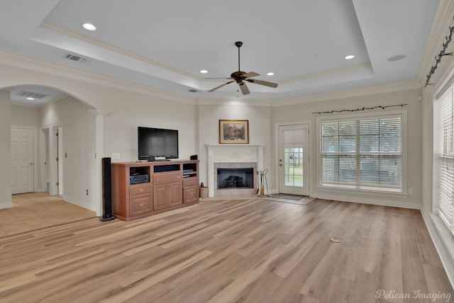 unfurnished living room featuring arched walkways, a tray ceiling, a tiled fireplace, and visible vents