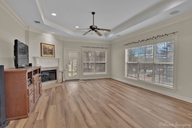 unfurnished living room featuring ceiling fan, a raised ceiling, light wood-style floors, a tile fireplace, and visible vents