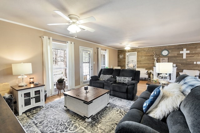 living area featuring light wood-type flooring, wood walls, crown molding, and a ceiling fan