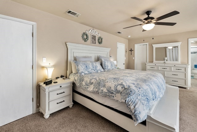 bedroom with a ceiling fan, light colored carpet, visible vents, and ensuite bath