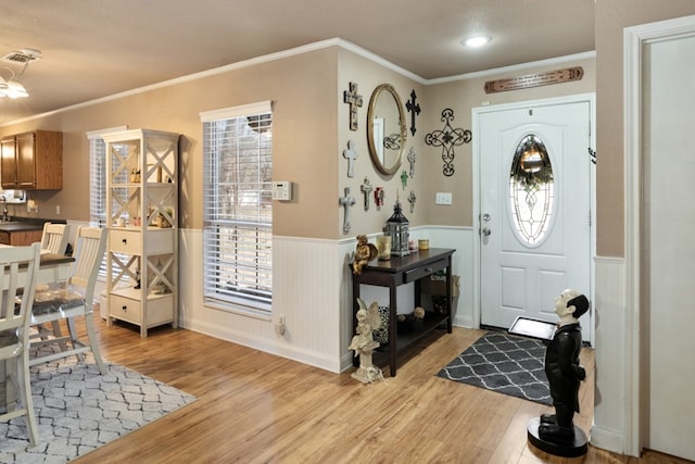 entryway featuring light wood-style floors, a wainscoted wall, crown molding, and visible vents