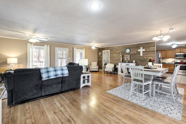 living area featuring ceiling fan with notable chandelier, light wood finished floors, and a textured ceiling