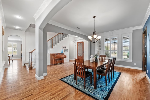 dining room with arched walkways, ornamental molding, stairway, and light wood-style floors