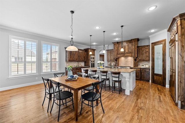 dining area with arched walkways, crown molding, light wood finished floors, recessed lighting, and baseboards