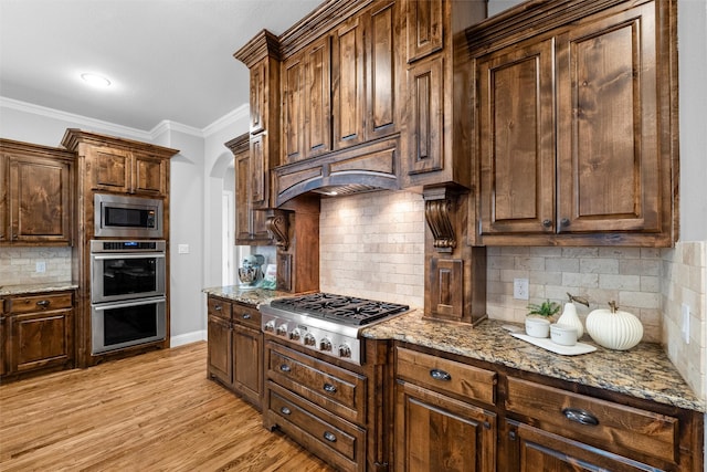 kitchen featuring baseboards, light wood-style flooring, ornamental molding, light stone counters, and stainless steel appliances